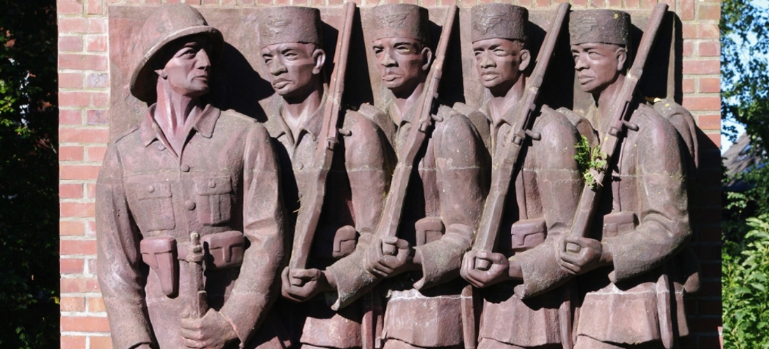 Das Foto zeigt die rechte Seite des Askari-Reliefs im Tansania-Park in Hamburg. Zu sehen ist auf dem Relief eindeutscher Offizier und vier bewaffnete Schwarze Soldaten in militärischer Uniform.