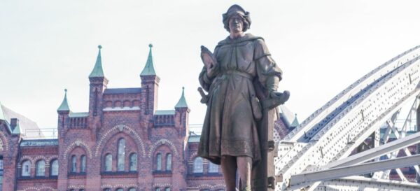Das Foto zeigt die Kolumbus-Statue in der Speicherstadt. Vor einer Brücke steht die Statue des Kolumbus auf einem Sockel.