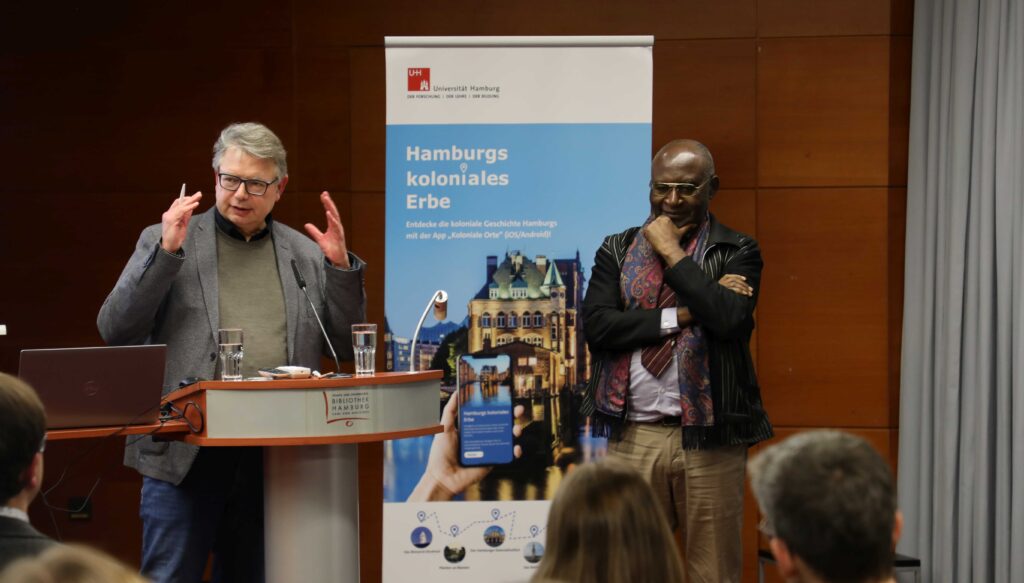 Prof. Dr. Jürgen Zimmerer (li.) begrüßt Prof. Dr. David Simo für seine Keynote „Die Entstehung von Kamerun als deutsches Kolonialprojekt: Voraussetzungen, Methoden und Konsequenzen“. Foto: Nils Lehmann/UHH